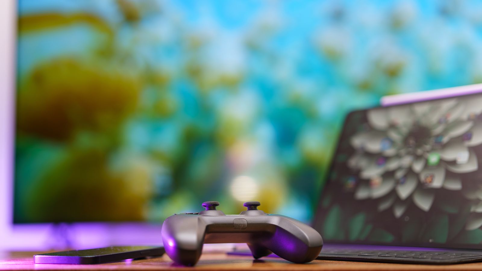 A modern gaming setup featuring a controller, laptop, and vibrant TV screen in a cozy home environment.