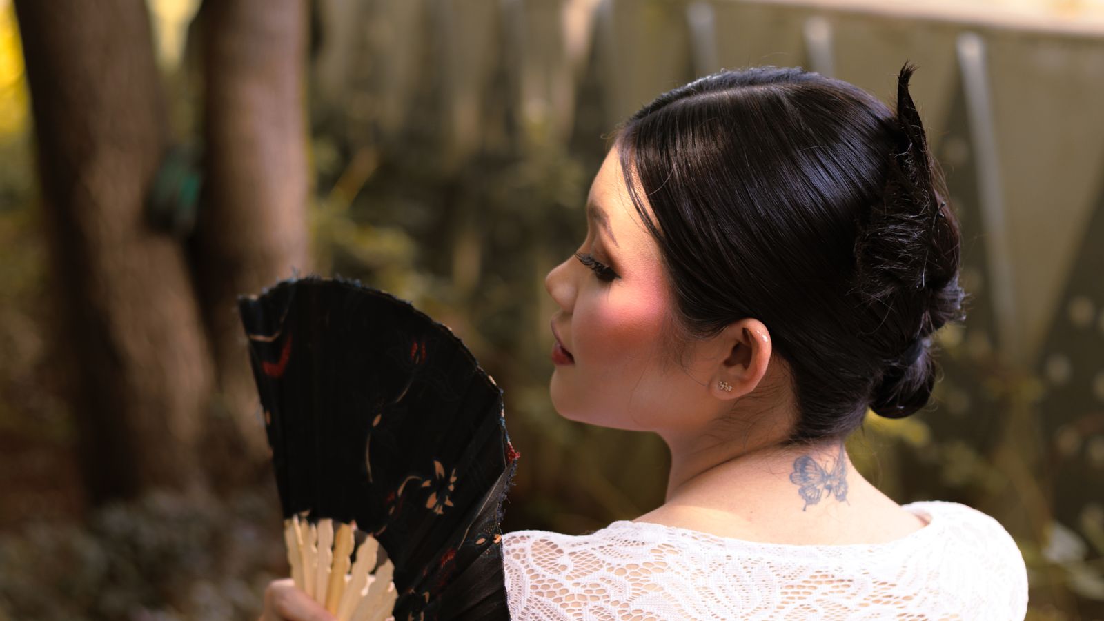 A woman holds a fan outdoors, showcasing elegance and traditional style.