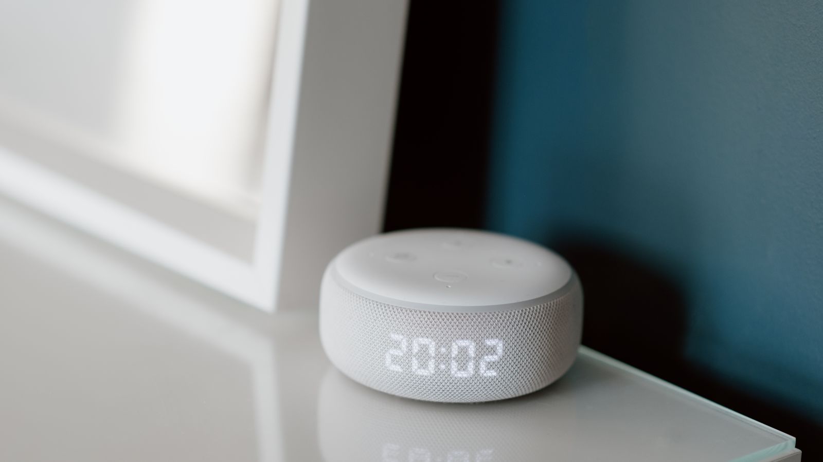 Close-up of a smart speaker with an illuminated 20:02 LED clock display on a desk.