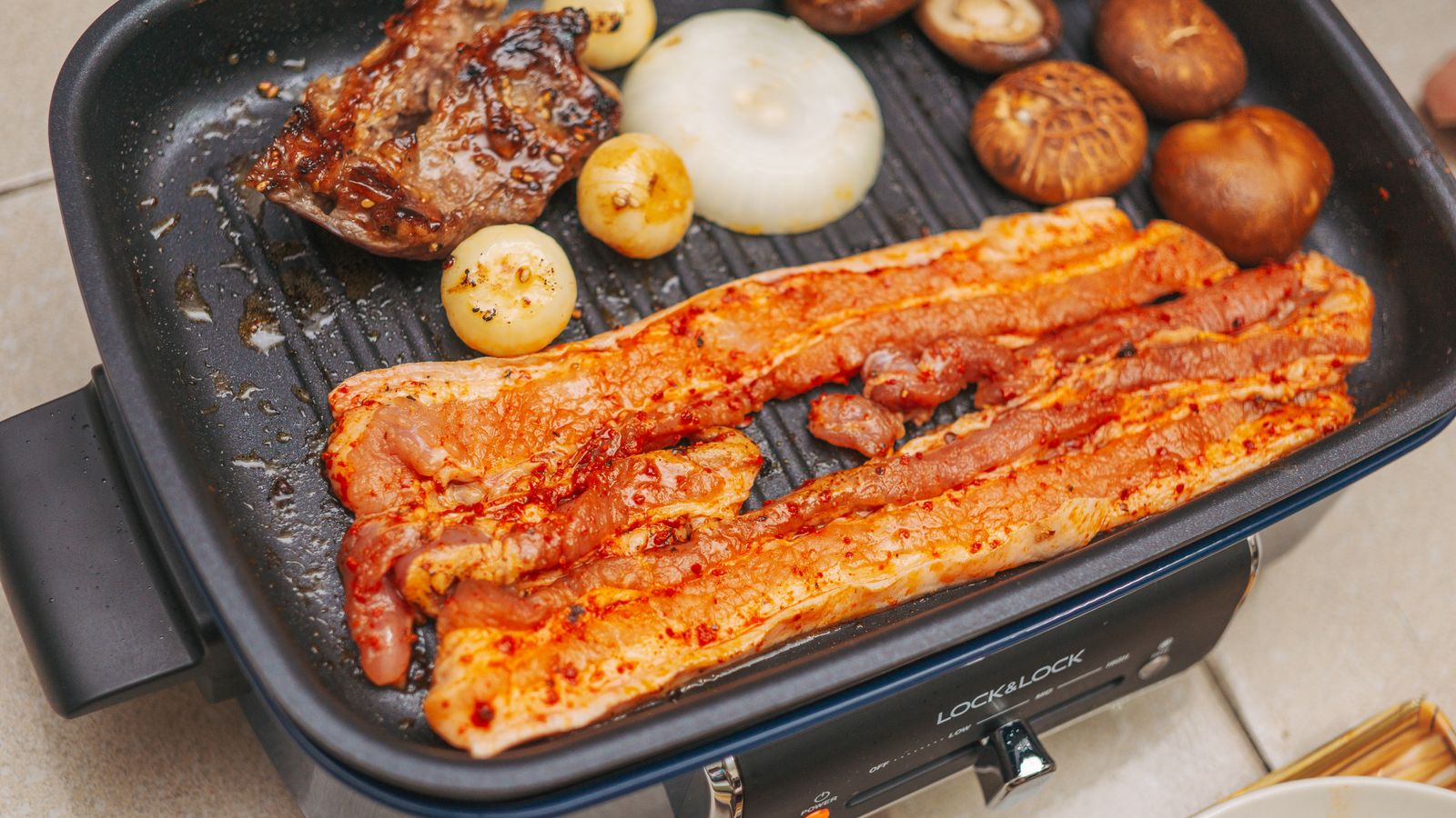 Close-up of pork belly and vegetables grilling on an electric pan for a delicious meal.