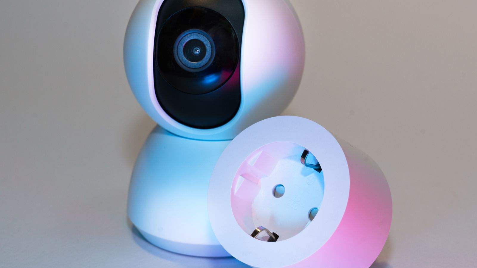 Smart home security camera and plug socket on a neutral background.