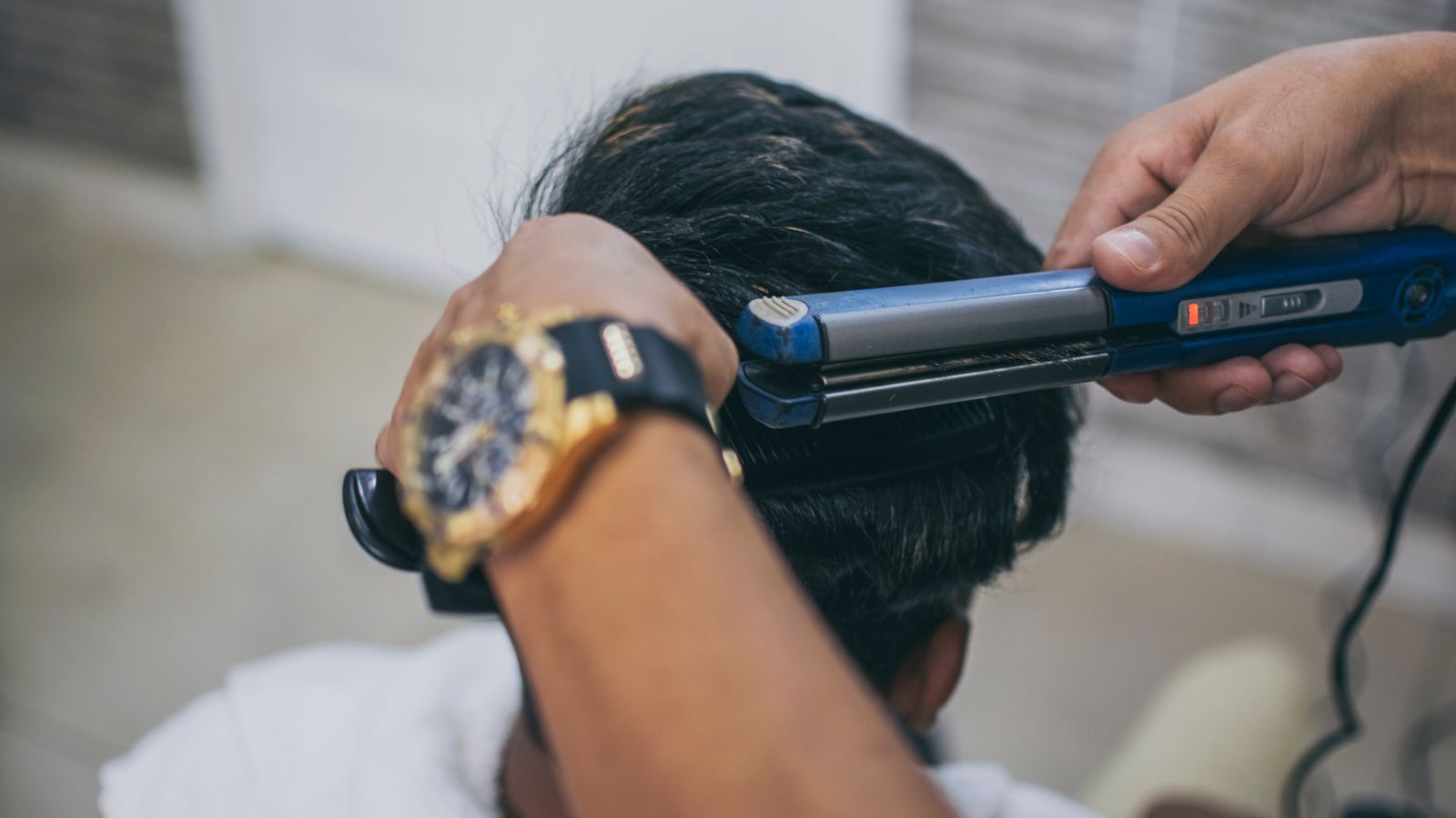 Close-up of a hairdresser styling a client's hair using a straightener in a barbershop.