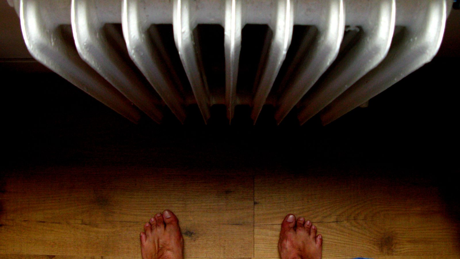 A unique perspective from above showing bare feet standing on wooden floor near a radiator.