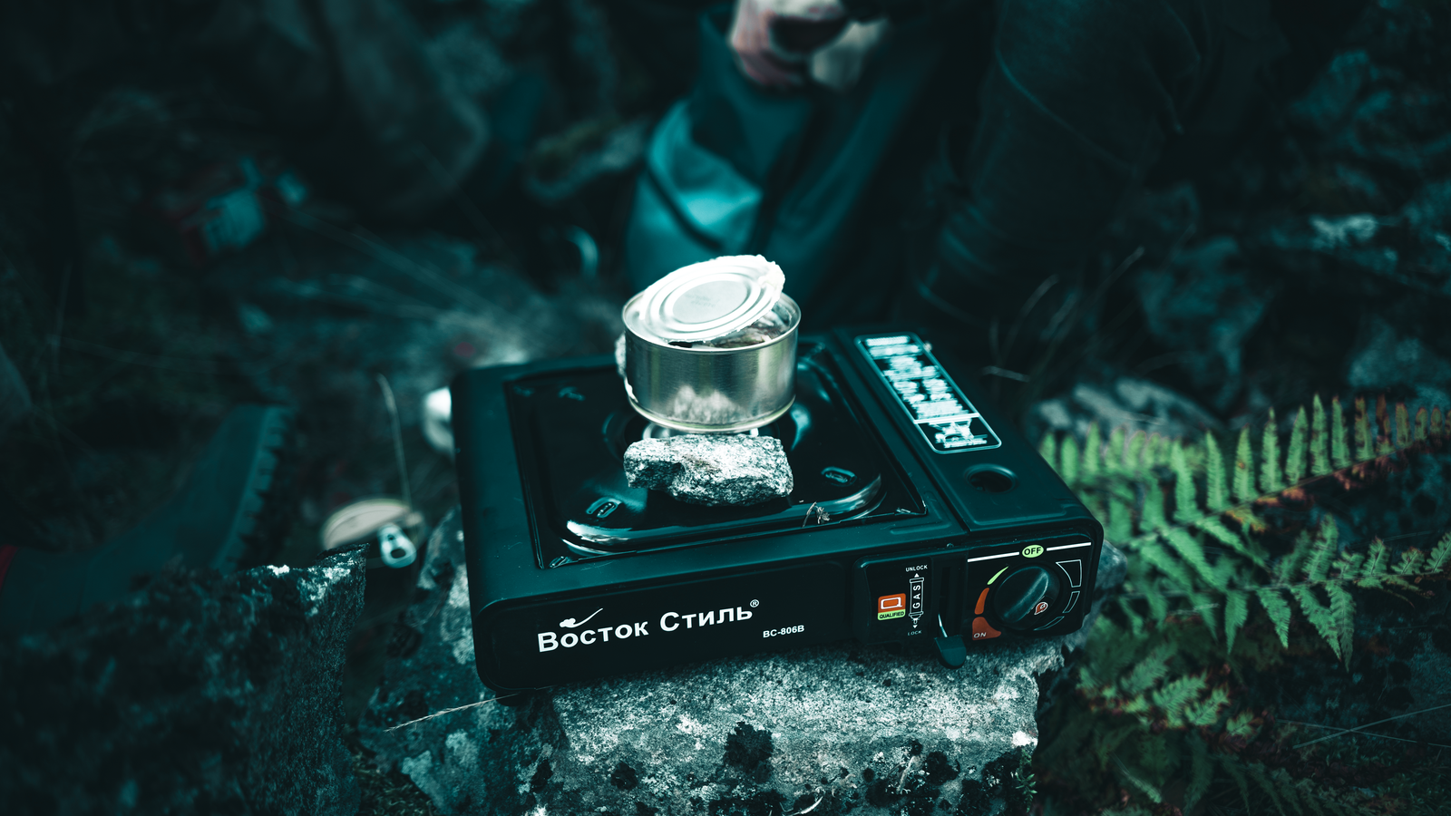 A portable gas stove heating a canned meal outdoors, perfect for camping.