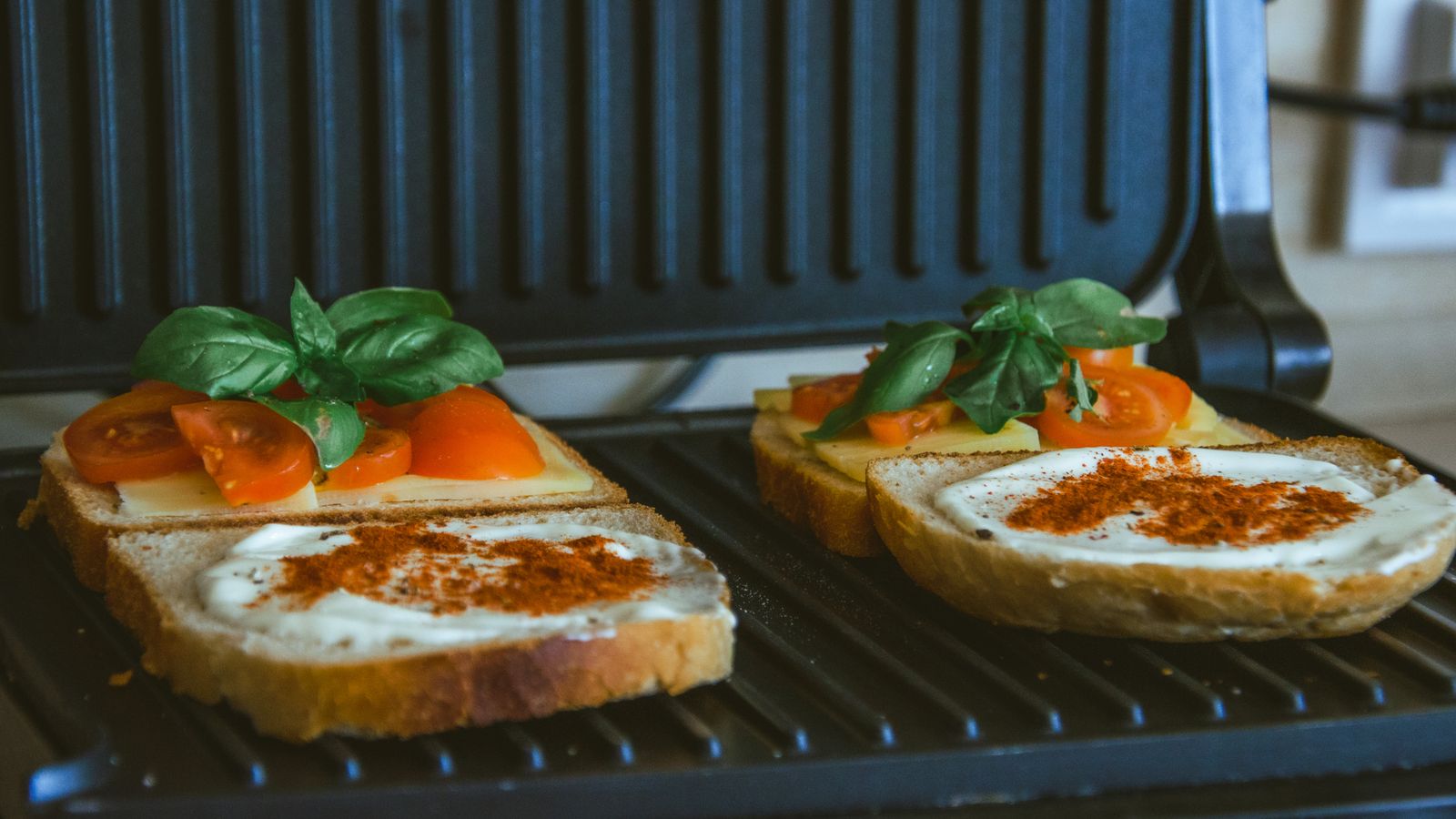 Close-up of a sandwich with cheese, tomatoes, and spices on a grill, showcasing fresh ingredients.