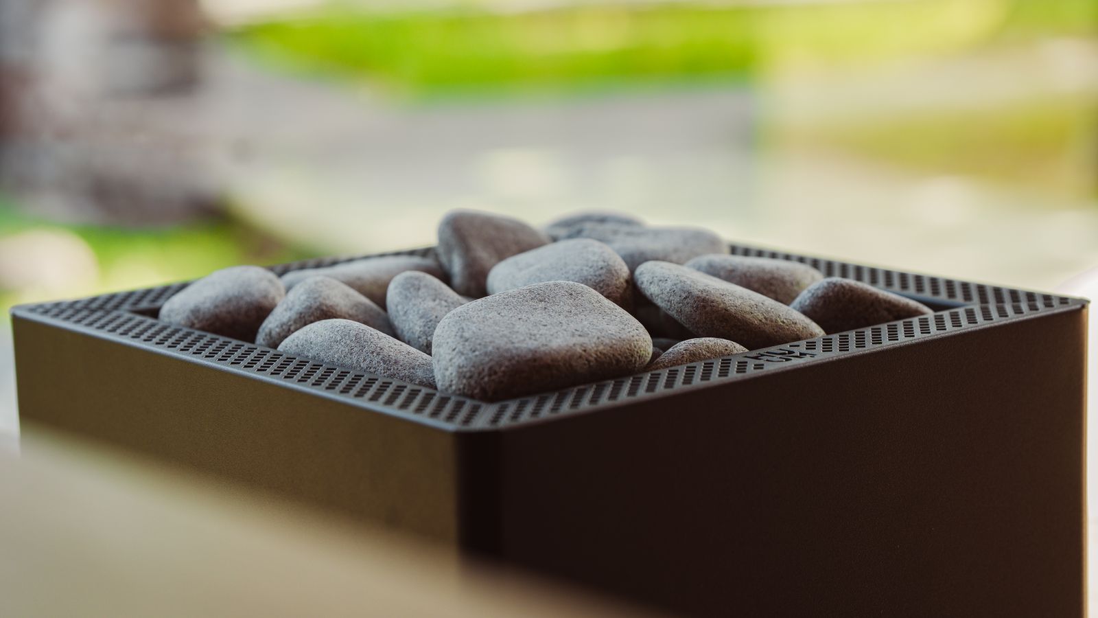 A modern sauna heater with smooth stones indoors, capturing a minimalist Nordic design aesthetic.