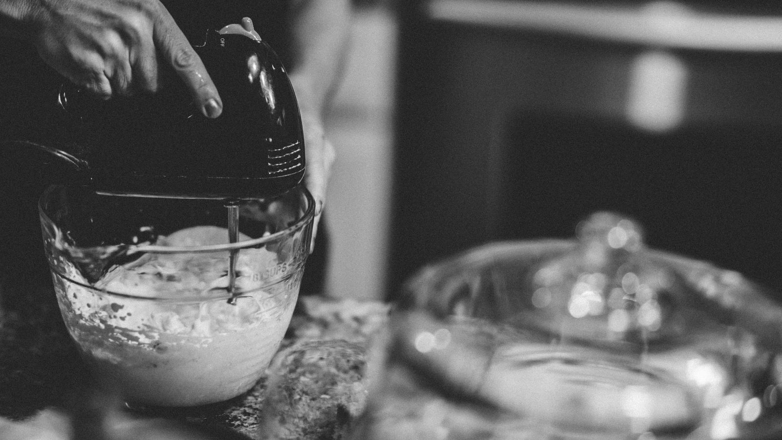 A hand using a mixer in a monochrome kitchen setting, creating a classic baking scene.