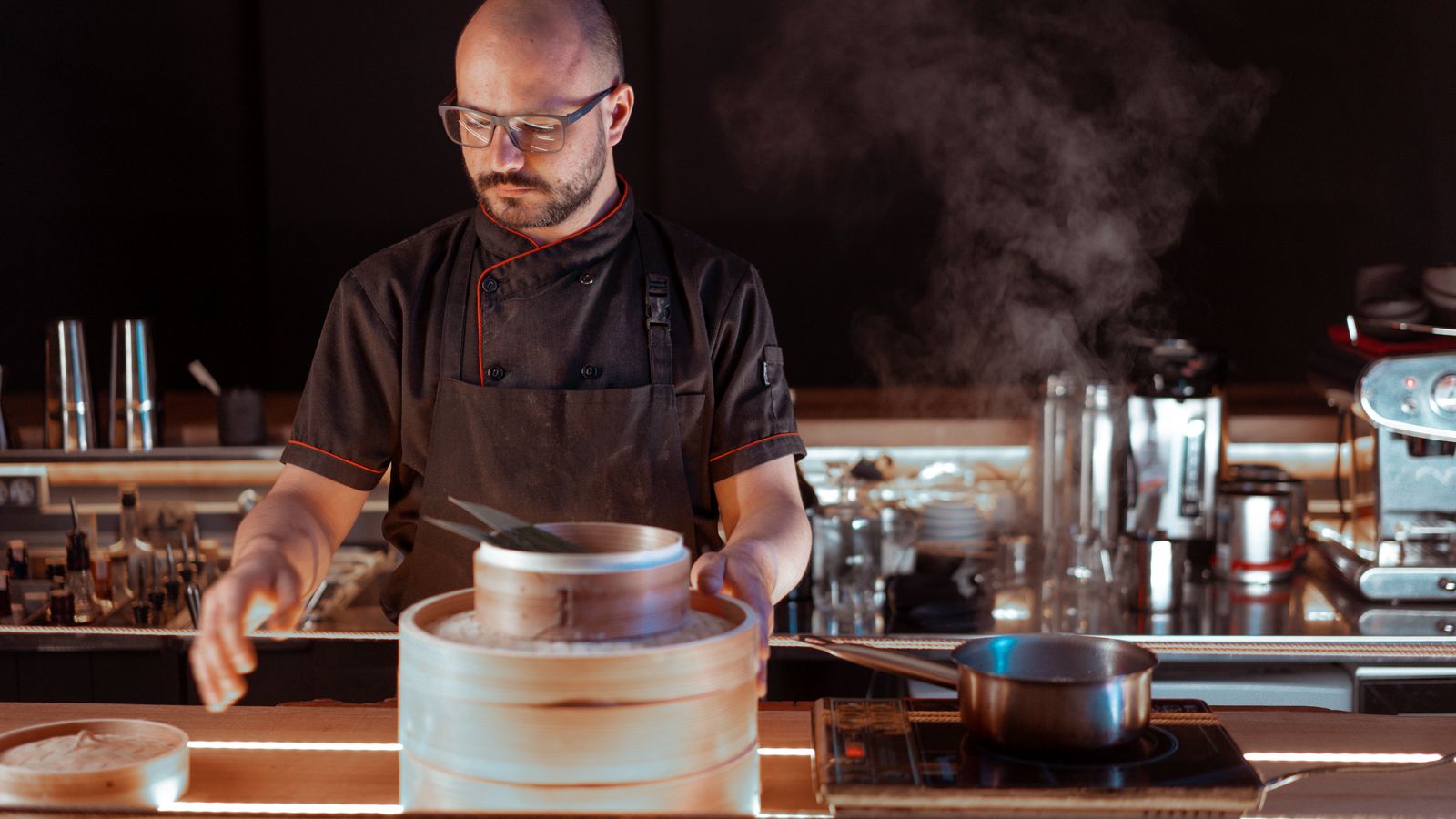 A skilled chef in a modern kitchen making dim sum with steam rising.