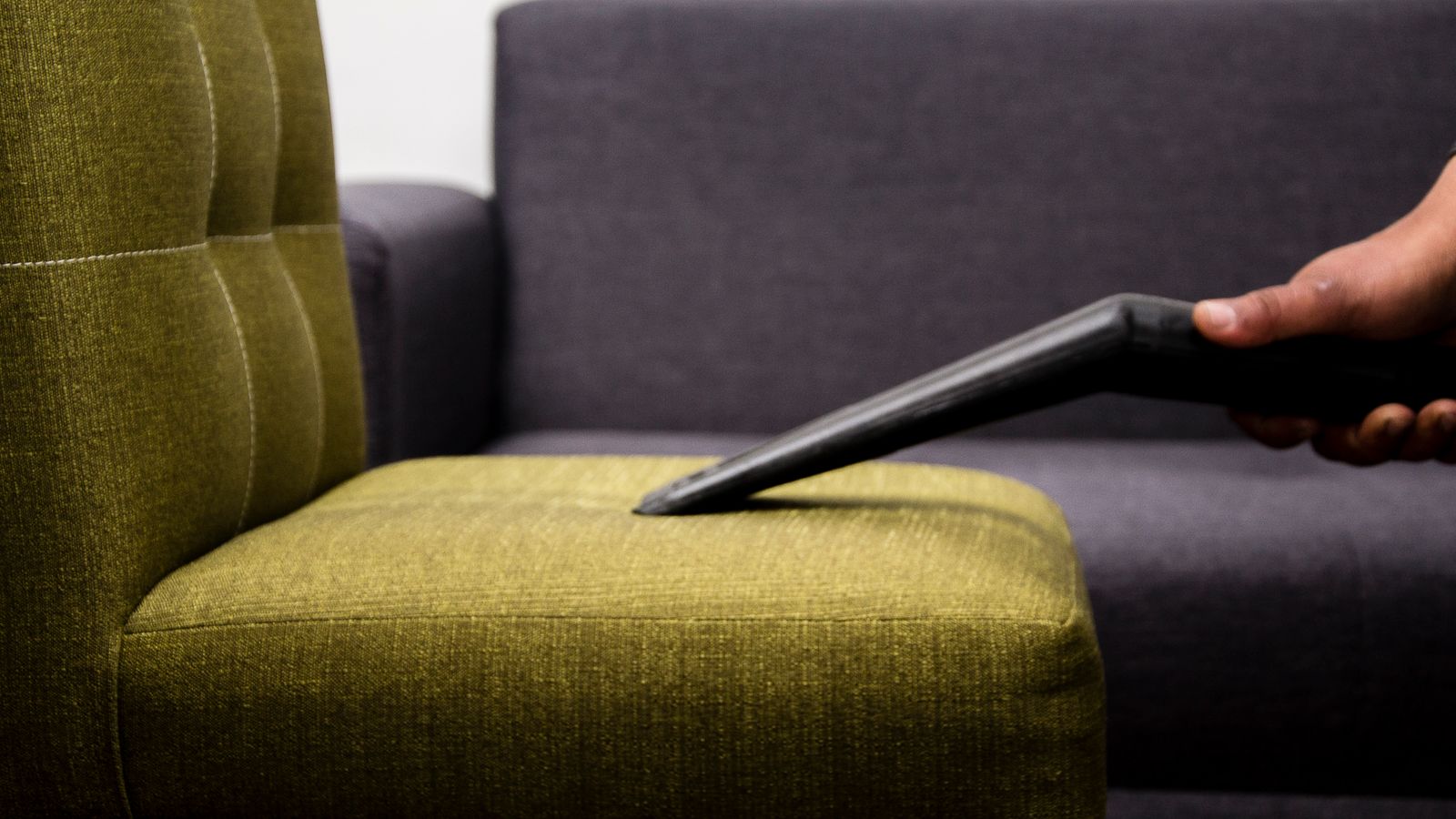 Close-up of a person vacuuming a modern sofa chair indoors, highlighting cleaning service.