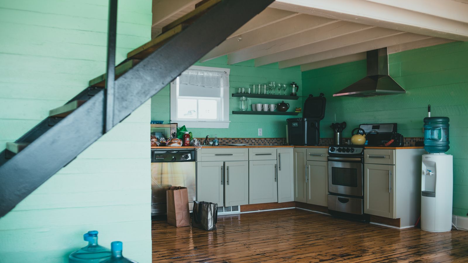 A cozy modern kitchen featuring green walls, wooden floor, and stainless steel appliances.