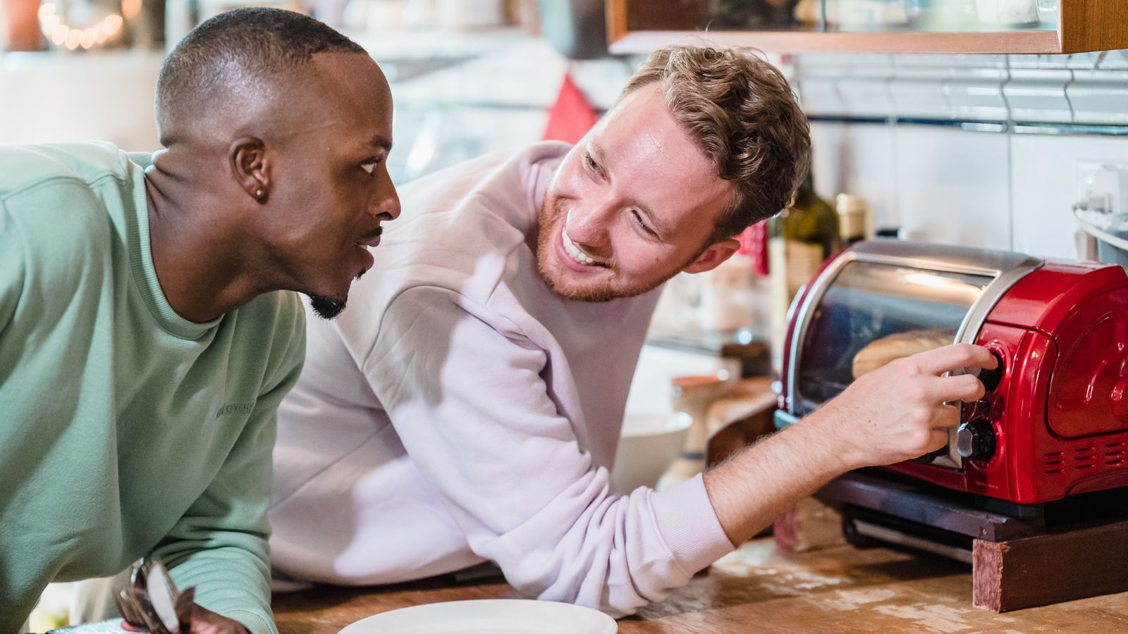 Two men sharing a joyful morning in a kitchen, preparing breakfast with smiles.