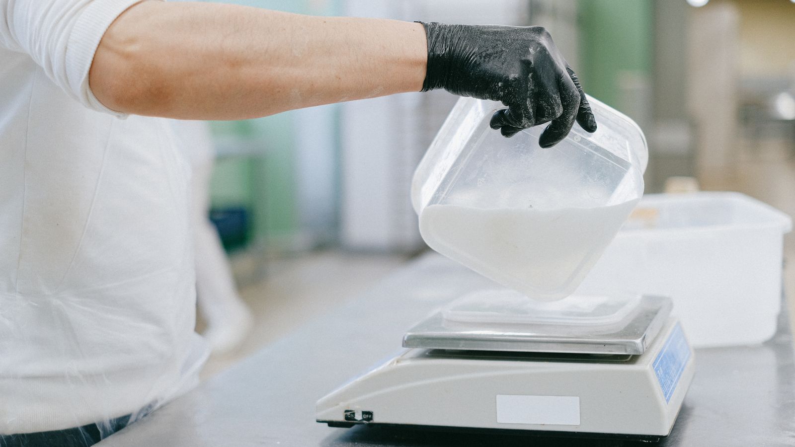 Chef in a kitchen carefully measuring ingredients using a digital scale.