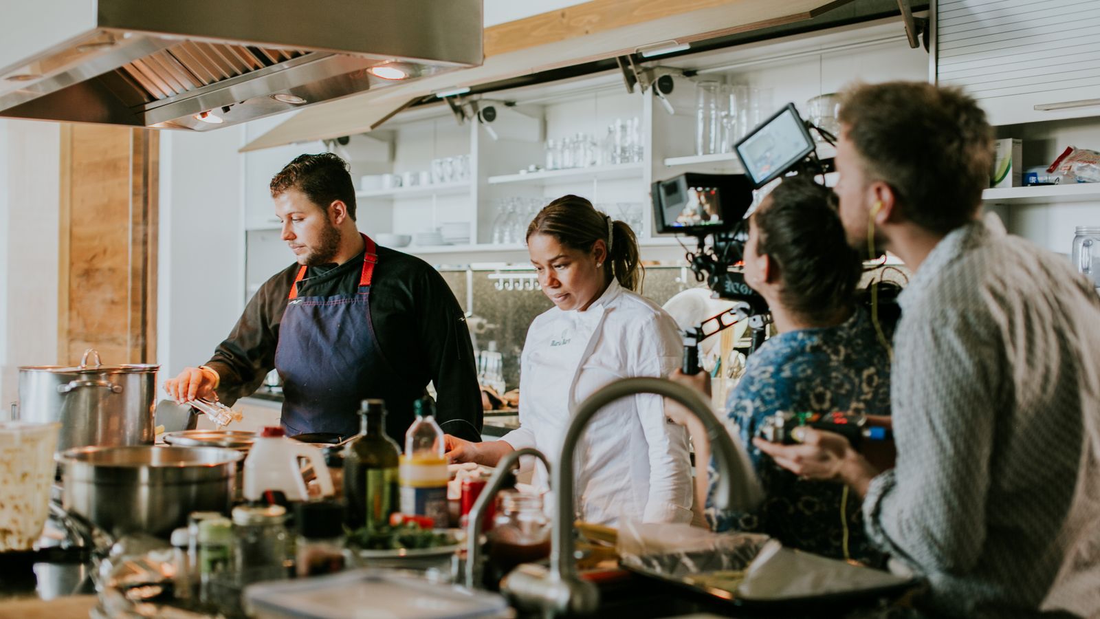 Chefs and camera crew collaborate in a modern kitchen for a culinary video shoot.