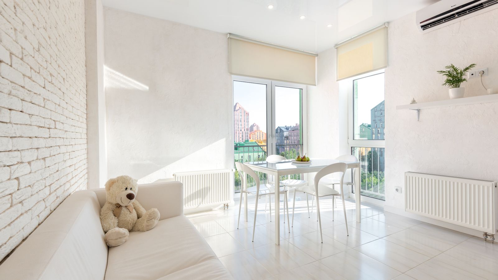 Interior of white kitchen furnished with sofa and chairs and table placed near big windows with blinds