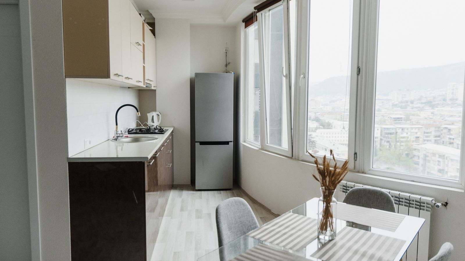 Bright modern kitchen with a glass table, minimalist design, and cityscape view through large windows.