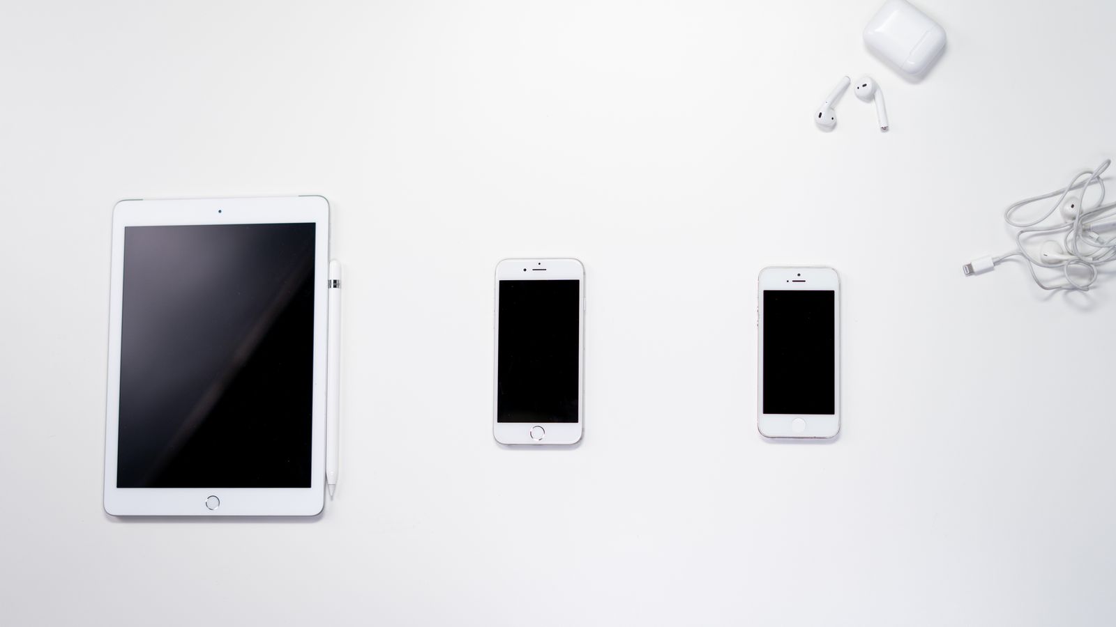 Flat lay of smartphone, tablet, and earphones arranged on a white surface for a clean, minimalist aesthetic.