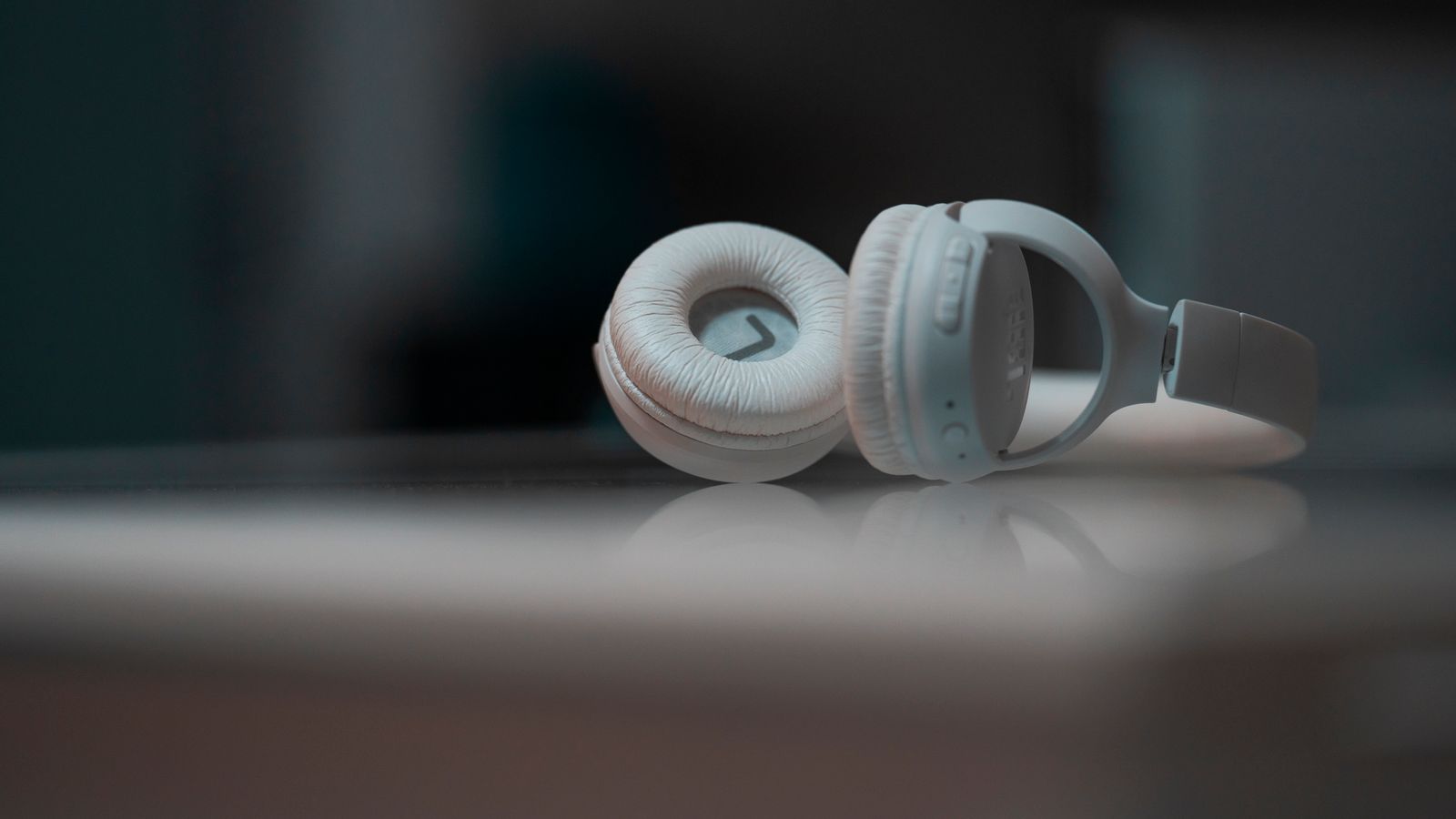Close-up view of white headphones on a reflective surface, showcasing modern audio technology.