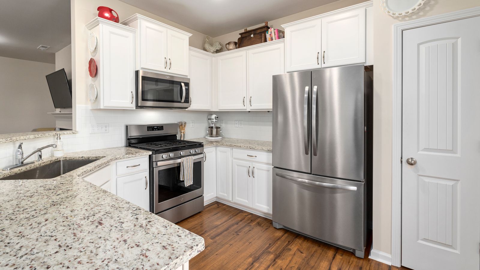 Bright modern kitchen featuring white cabinets and stainless steel appliances, including a refrigerator and stove.